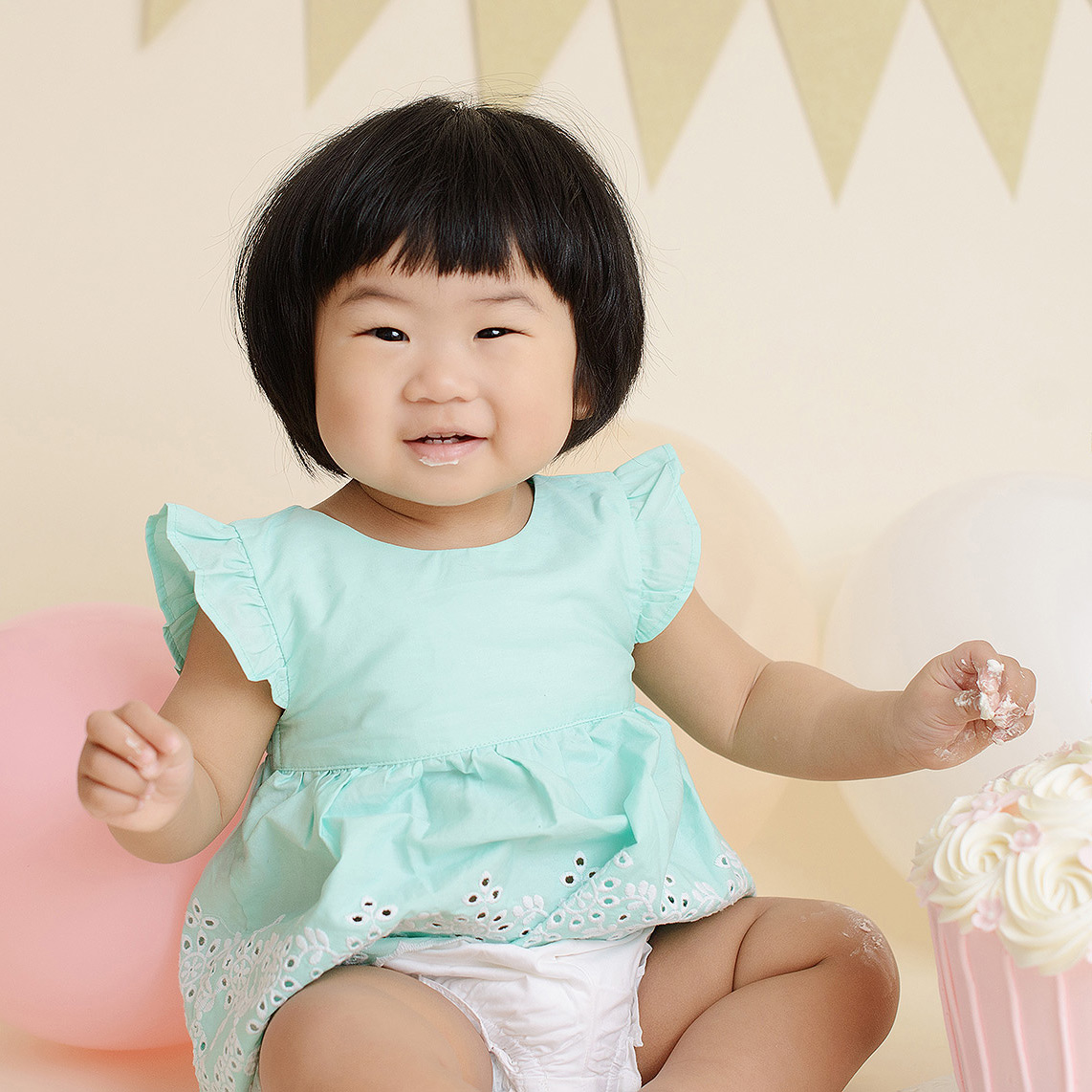 Baby girl with frosting on hands cake smash with balloon background