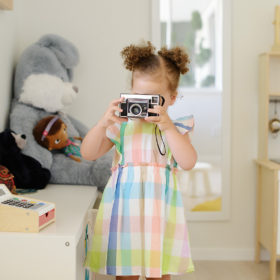 Toddler girl taking a photo in her playroom wearing plaid dress