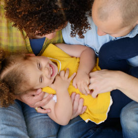 Mom and dad tickle and laugh with daughter wearing yellow