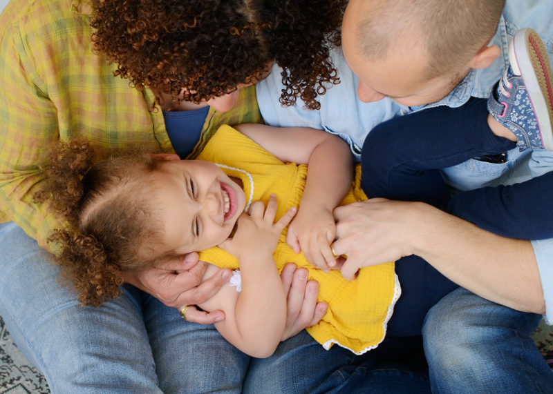 Mom and dad tickle and laugh with daughter wearing yellow