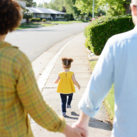 Toddler girl running in front of mom and dad as they hold hands outside of their home in Sacramento