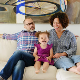 Family photo on the couch with toddler girl laughing