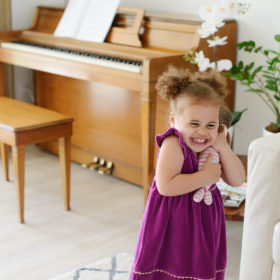 Toddler girl laughing and hugging toy with piano in background
