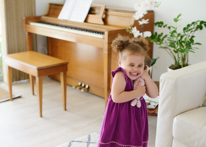 Toddler girl laughing and hugging toy with piano in background