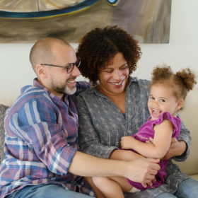 Mixed race parents hugging their daughter on the couch and smiling