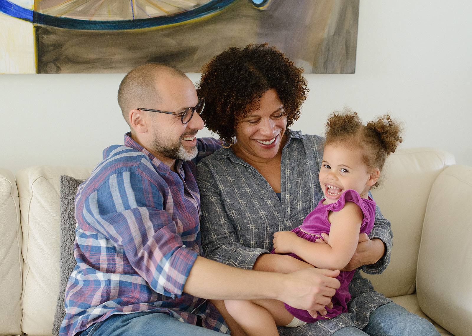 Mixed race parents hugging their daughter on the couch and smiling