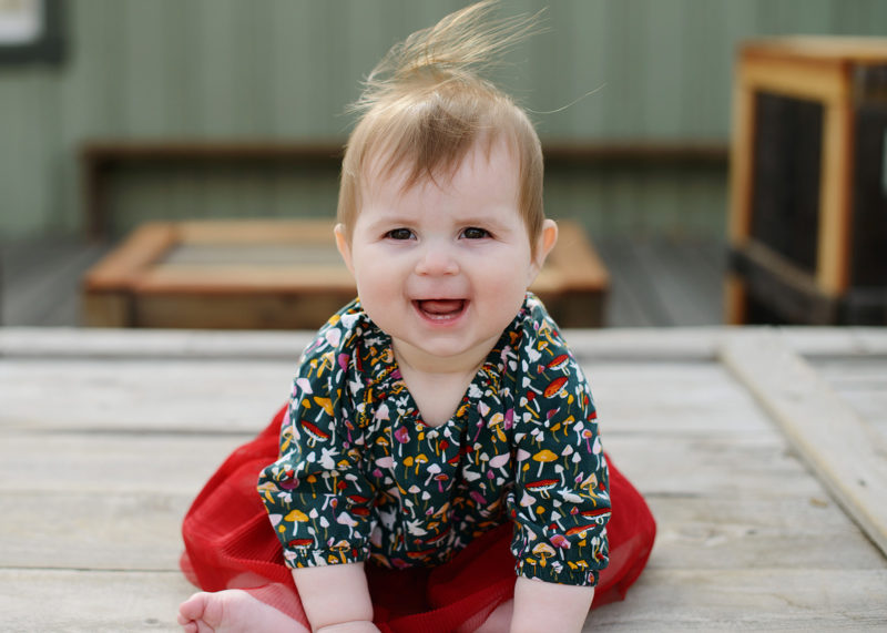 Baby girl smiling and sitting up wearing red skirt in Old Sacramento