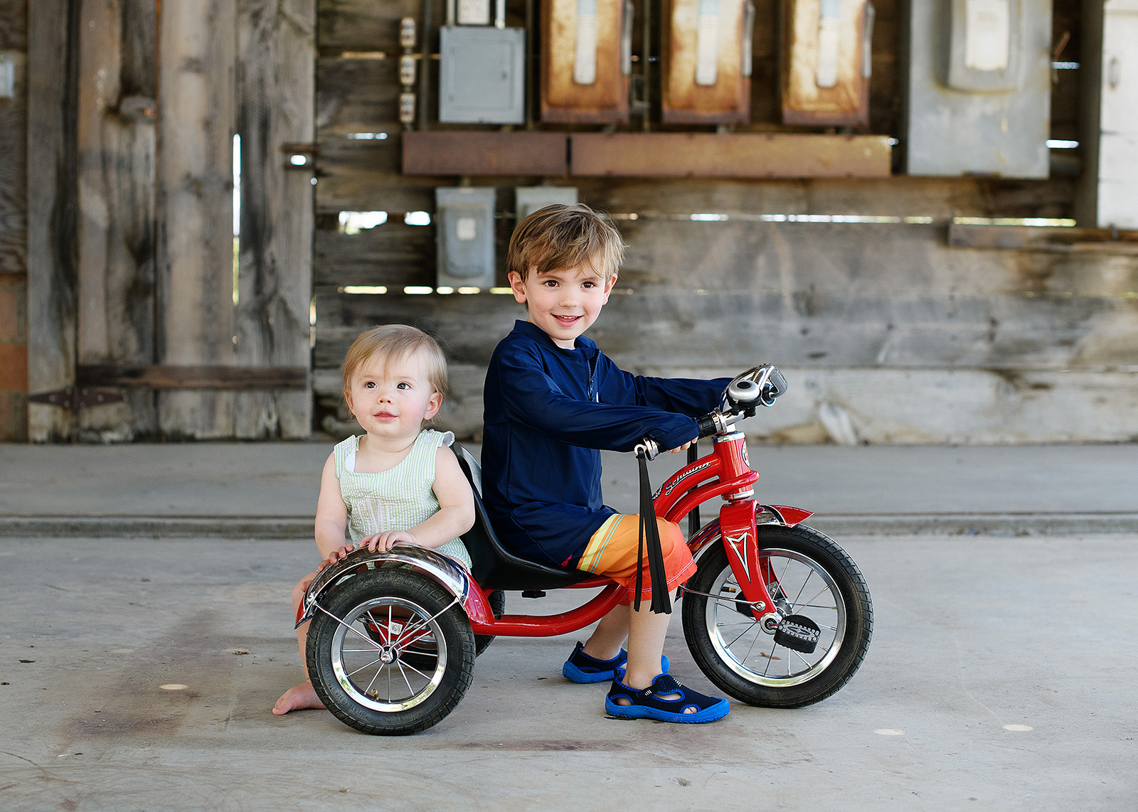 Brothers riding on red tricycle at first birthday party on farm