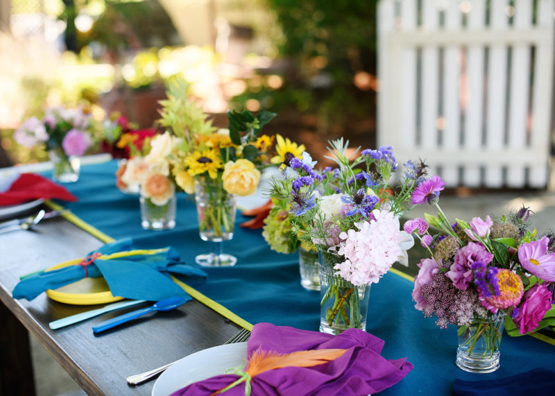 First birthday party tablescape with bright floral arrangements and napkins