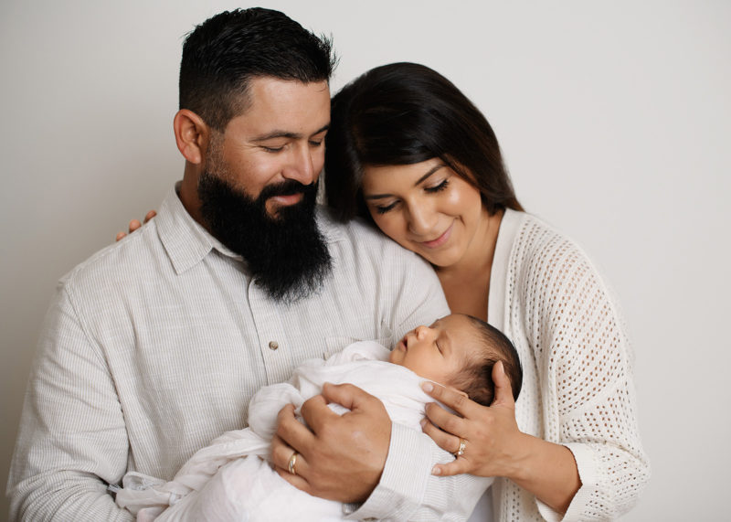 Mom and dad snuggle up to newborn baby wearing neutrals in studio