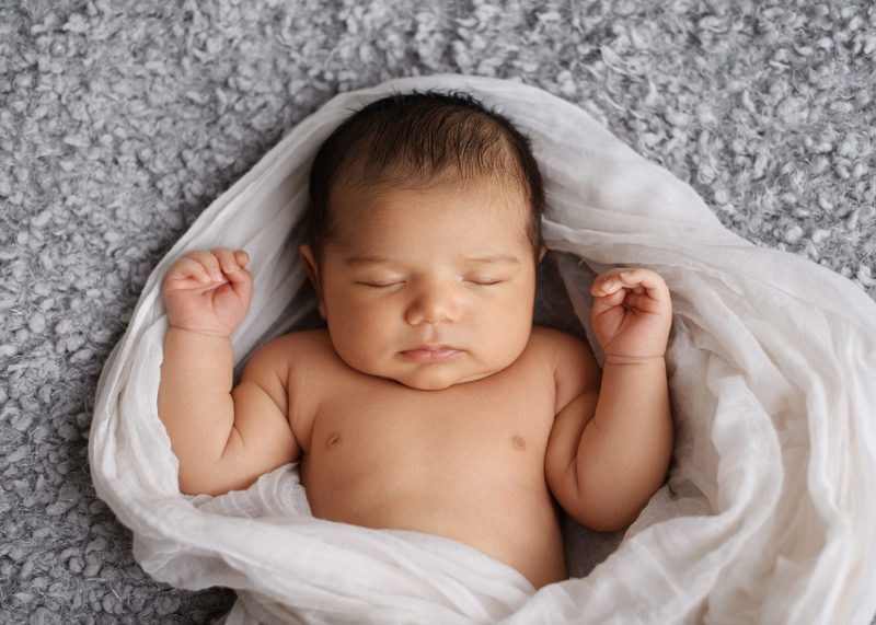 Newborn baby in muslin swaddle in studio