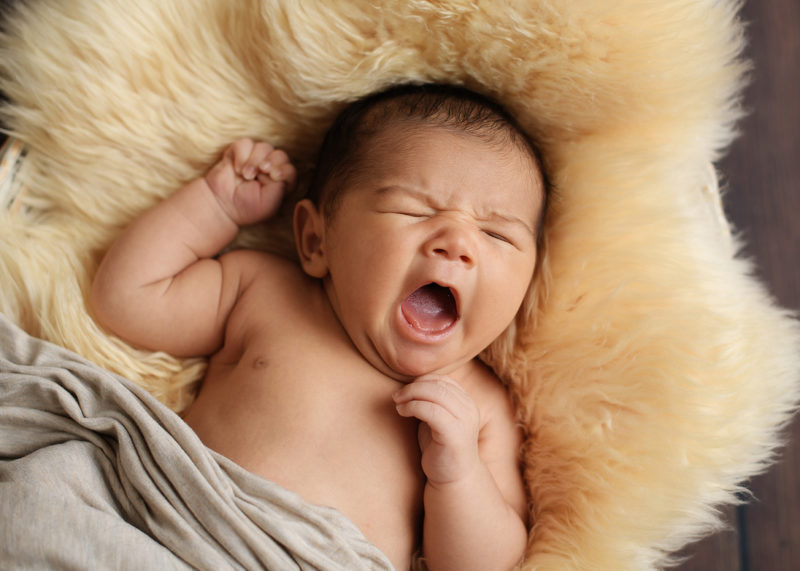 Newborn baby yawns on fuzzy throw blanket