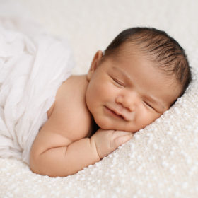 Newborn baby smiles as he sleeps on cozy white blanket