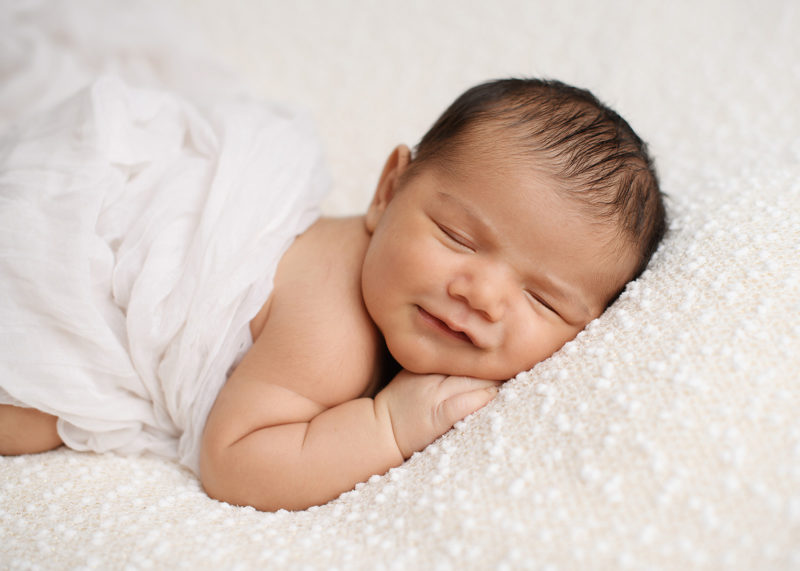 Newborn baby smiles as he sleeps on cozy white blanket
