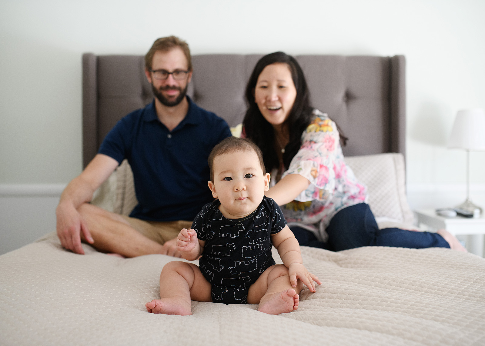 Lifestyle session in home on bed with 6 month baby boy in foreground and parents in background