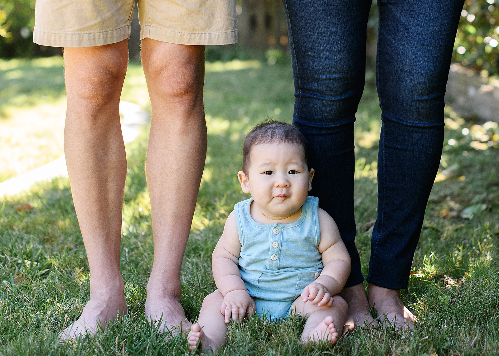 6 month baby boy sitting on grass next to mom and dad's feet in Sacramento backyard