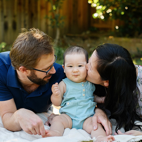 Mom kissing 6 month old baby boy on picnic blanket in yard