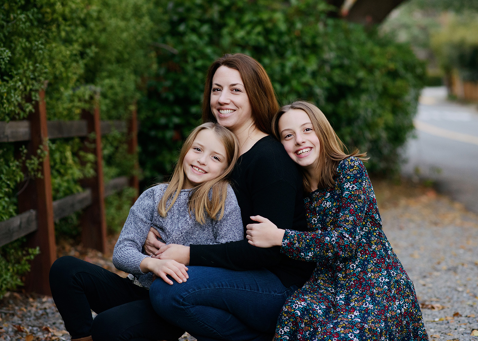 Mom and daughters hugging outdoors near trees in Saratoga