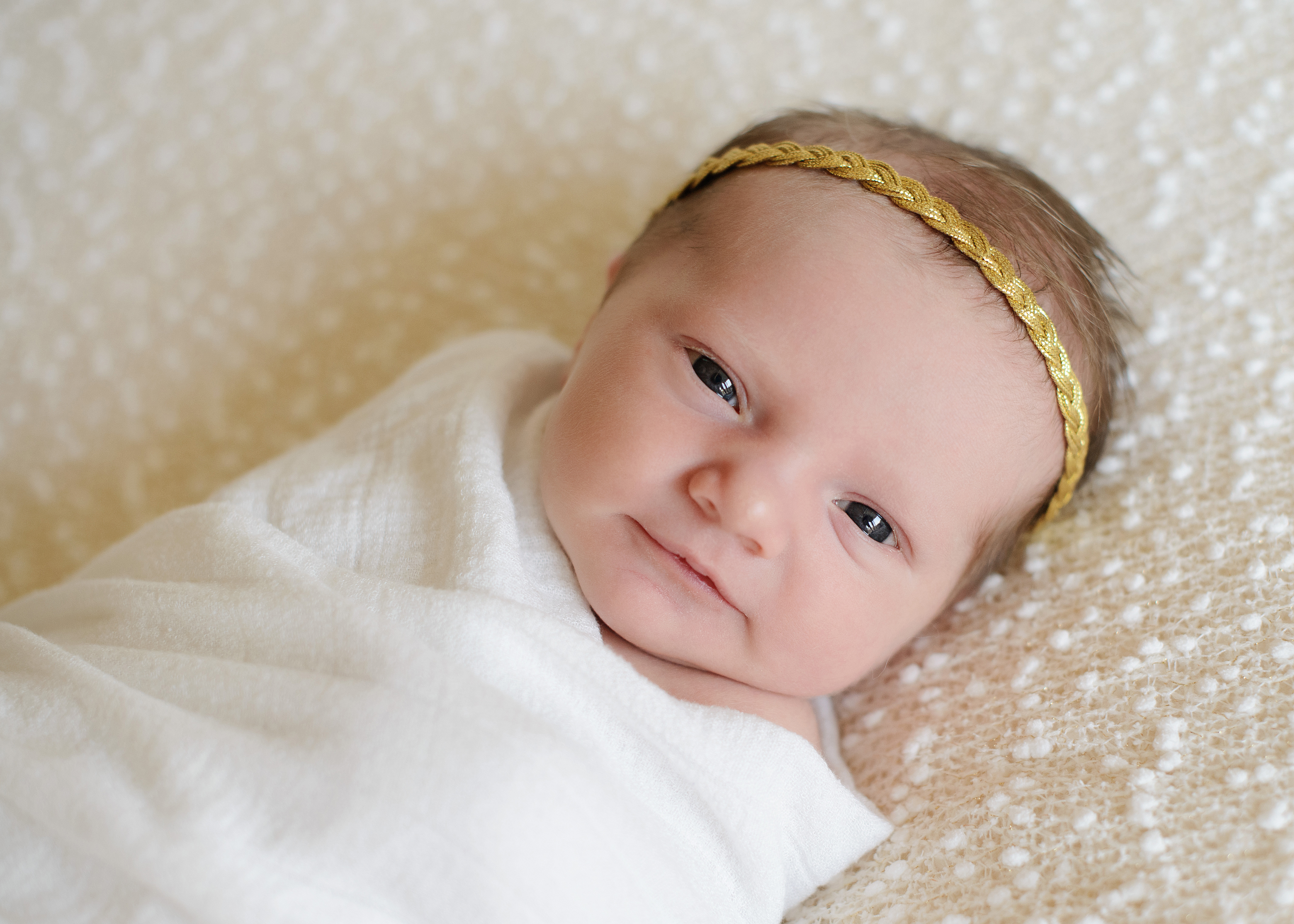 Newborn baby girl in gold headband on white blanket and swaddle