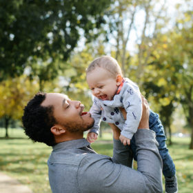Dad smiling and lifting up baby boy in Sacramento outdoors