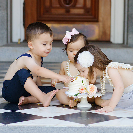 Big sister puts face in cake with brother and sister looking on at State Capitol