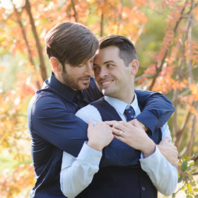 Same sex couple in a loving embrace with orange autumn leaves in background in Fair Oaks
