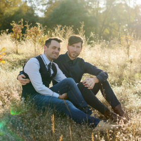 Gay male couple sitting in an embrace on golden grass in Fair Oaks