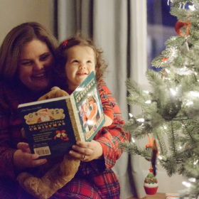 Mom reading The Night Before Christmas book to daughter by Christmas tree