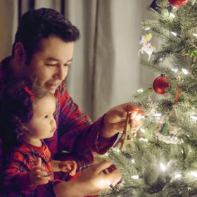 Father and daughter in matching pajamas putting ornaments on Christmas tree