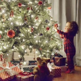 Toddler girl in pajamas reaching for Christmas tree ornament