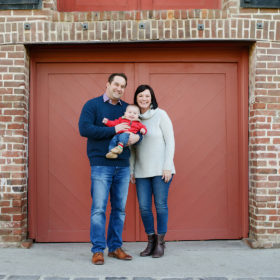Mom and dad holding baby boy in front of red brick background in Old Sacramento