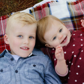 Big brother and little sister cuddling on flannel blanket and looking at camera