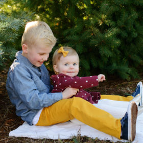 Big brother and little sister cuddling on blanket by pine trees
