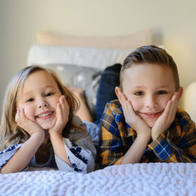 Sister and brother on bed smiling at camera in Sacramento