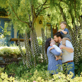 Parents kiss as they hold sons in front lawn greenery Sacramento