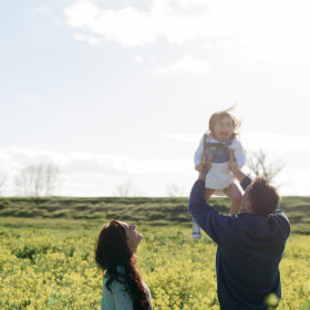 Dad lifting up toddler daughter to the sky in middle of flower field in West Sacramento