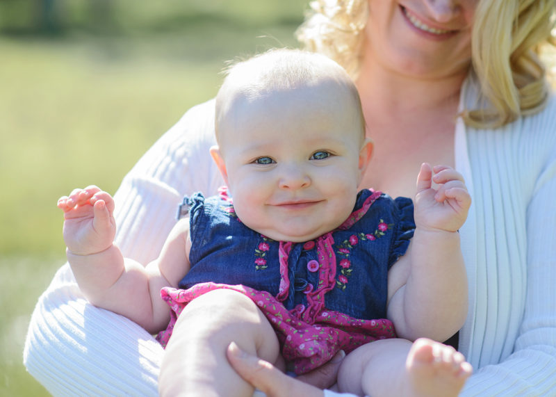 6 month baby girl smiling directly into camera as mom holds her