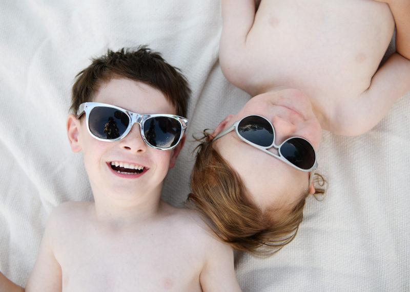 Brothers wearing sunglasses while lying on beach towel at Folsom Lake State Recreation Area