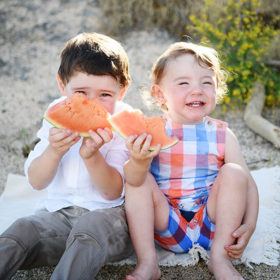 Brothers smiling and eating watermelon on beach sitting on sand in Folsom Lake