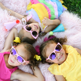 Little girls wearing sunglasses lying down on pink fluffy rug