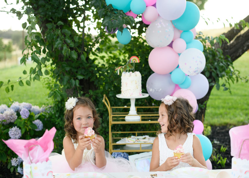 Little girl eating a cupcake with balloon arch and unicorn cake in backdrop
