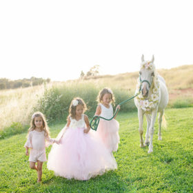 Girls wearing pink tutus walking beside a white horse on meadow