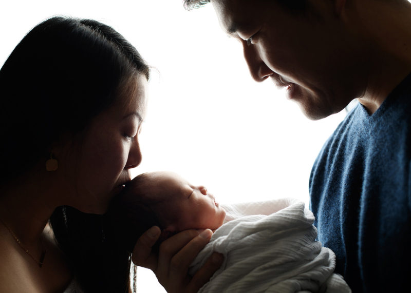 Silhouette of mom and dad kissing newborn baby's head