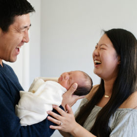 Mom and dad laugh while holding newborn baby girl