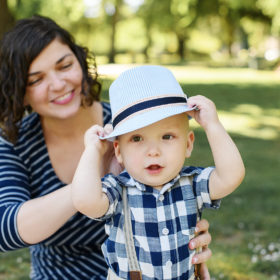 One year old boy wearing straw fedora and blue checkered shirt as mom holds him in McKinley Park
