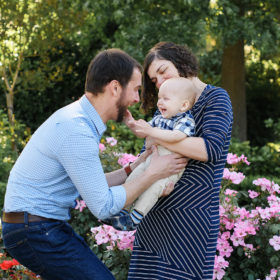 Dad tickling baby boy as mom smiles in McKinley Park Rose Garden
