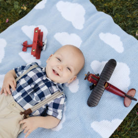 One year old boy smiling directly at camera with lying down on cloud blanket with red vintage airplanes