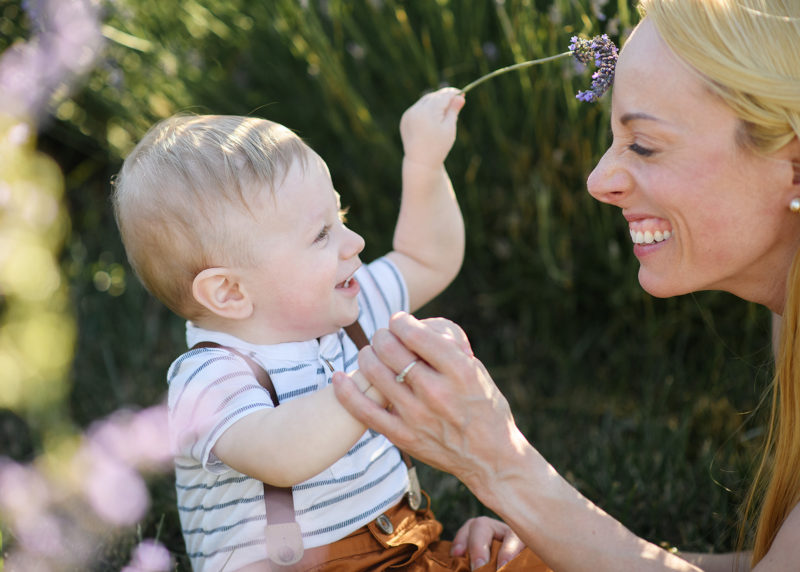Sacramento photographer, Jill Carmel, photographing one year old boy holding sprig of lavender and making mom laugh in Dixon