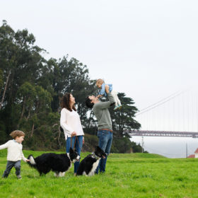 Family photo with dad holding up baby girl high in front of Golden Gate Bridge in Crissy Field