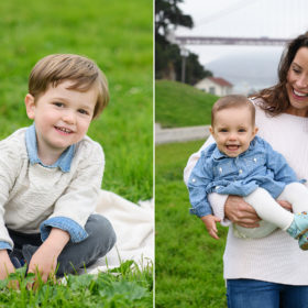 Toddler boy sitting on blanket on grass and mom holding baby girl in front of Golden Gate Bridge in Crissy Field